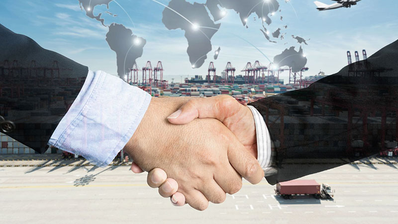 Business handshake with global map overlay and cargo ship, representing international logistics and engine supplier partnerships.