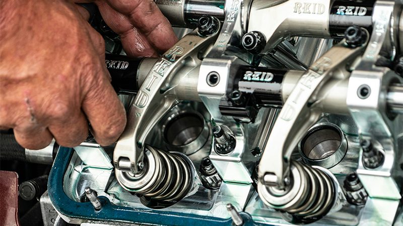 Mechanic working on a camshaft and engine valves, inspecting and adjusting engine components.