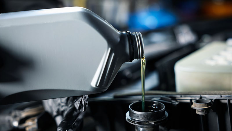 Adding engine oil from bottle into car engine for routine maintenance.