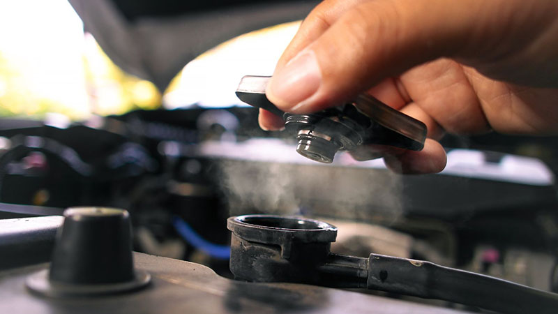 Mechanic opening radiator cap on overheated car engine.