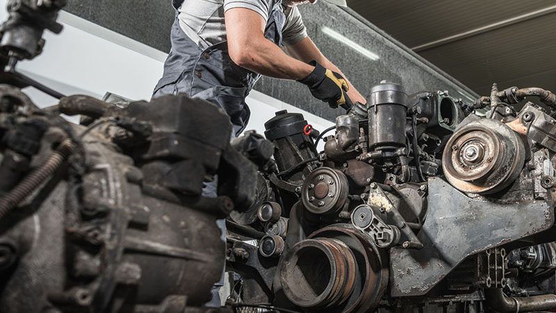 Truck mechanic rebuilding a heavy-duty diesel engine in a repair shop.