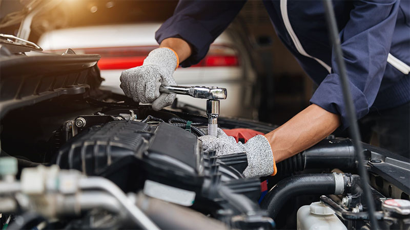Automotive mechanic repairing a car engine in a workshop with a wrench.
