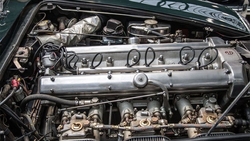 Крупный план старинного двигателя Aston Martin, демонстрирующий классическую топливную систему и механические детали.