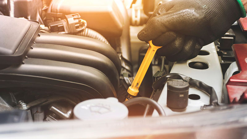 Mechanic pulling the oil dipstick from a car engine to check the oil level.