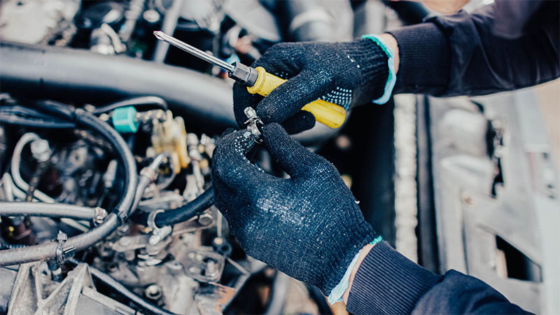 Mechanic replacing a fuel system hose in a car engine bay.