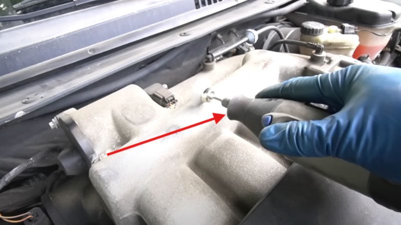 Using a rotary tool to scrub metal intake in the engine bay.