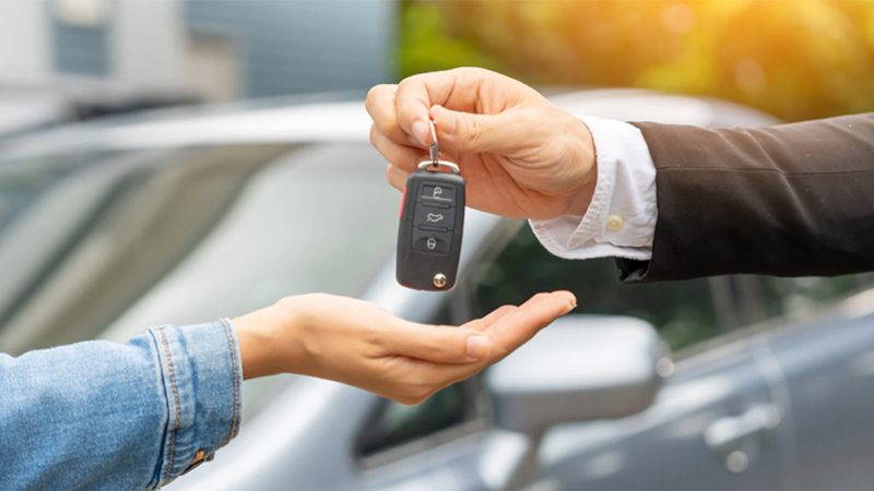 Man handing car key to another person, symbolizing the transfer of car ownership.