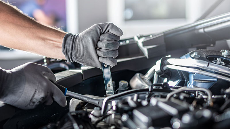 Auto mechanic repairing a car engine in a workshop setting.