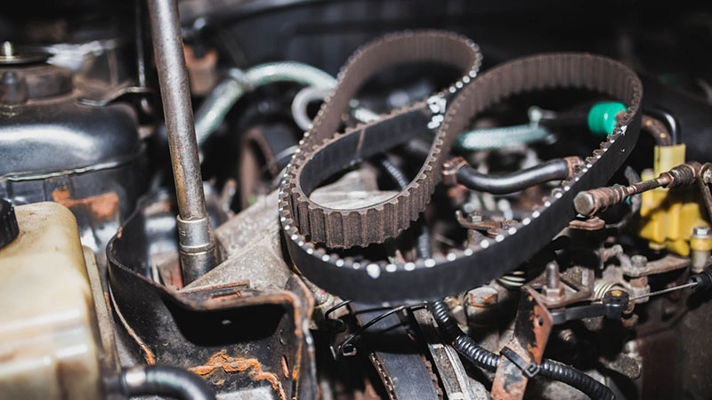 Mechanic replacing a timing belt on a car engine in a workshop.