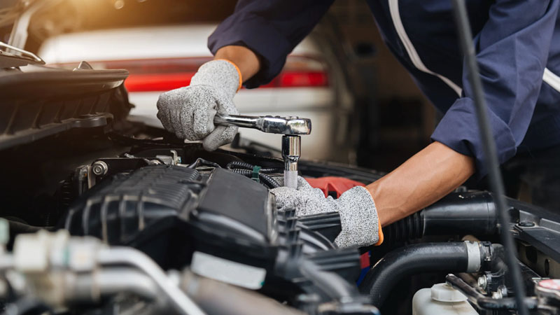 Automotive mechanic using a wrench to repair a car engine in a professional auto repair workshop.