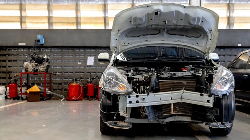 Car in an automobile repair service with the hood lifted up, showing the engine bay during maintenance or repair.