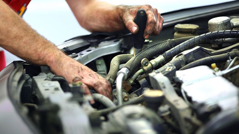 Close-up of an unrecognizable mechanic repairing a broken car engine in a workshop.