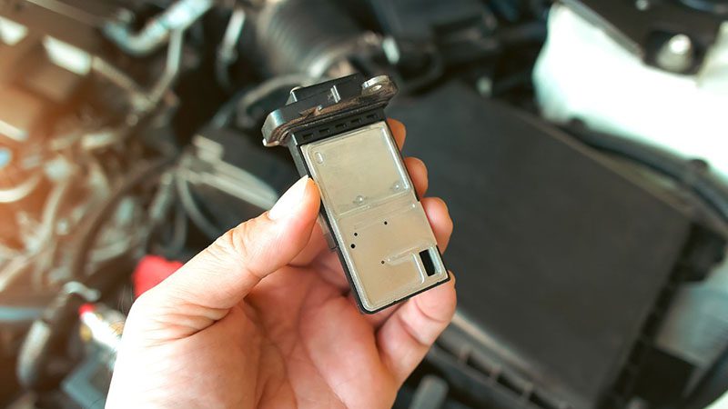 Hand holding a Mass Air Flow (MAF) sensor close-up, used in automotive engine systems