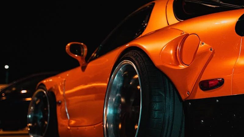 Gros plan dynamique d'une voiture de sport Mazda orange avec des modifications personnalisées, capturée la nuit.