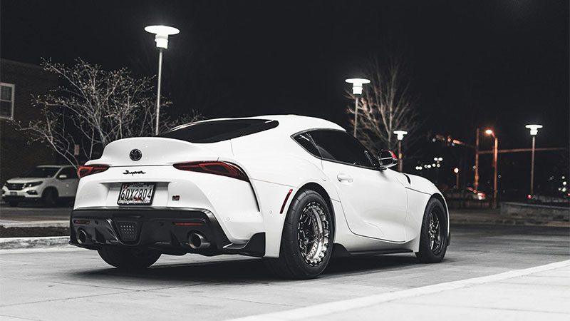 A sleek white Toyota Supra with custom rims parked in an urban setting at night.