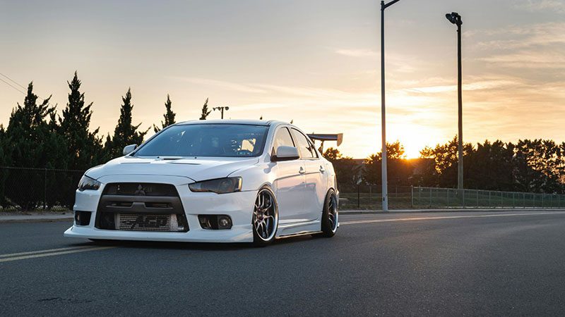 A white Mitsubishi car driving on the road, captured from a side angle during daylight.