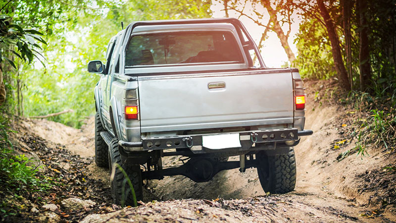 Four-wheel drive vehicle climbing difficult off-road terrain in forest.