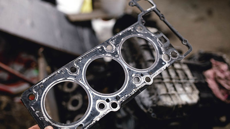 Механик заменяет прокладку головки блока цилиндров на двигателе автомобиля в гараже.