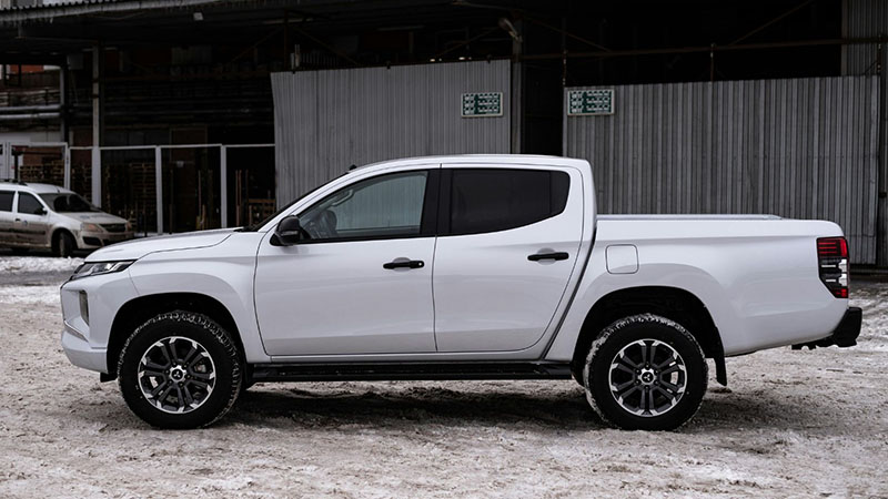 Белый пикап Mitsubishi Triton едет по промышленной зоне.