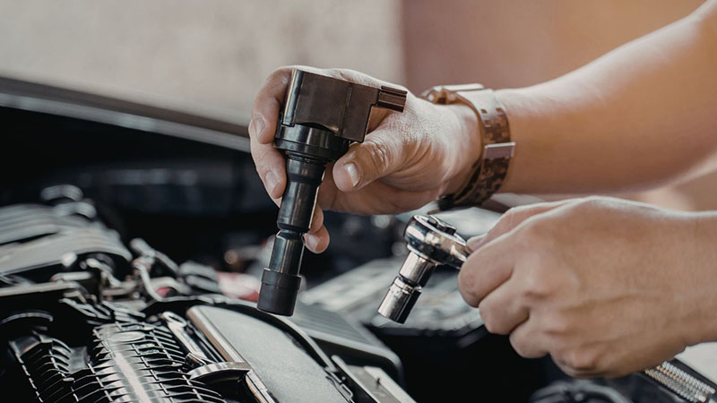 Mechanic replacing car ignition coil during engine repair.