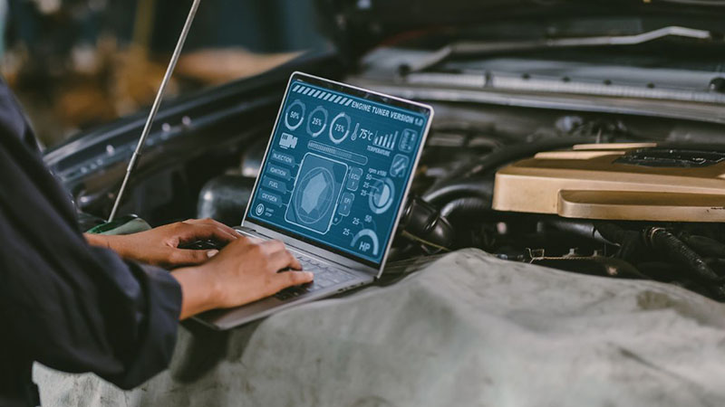 Auto technician checking engine ECU and combustion system with laptop.