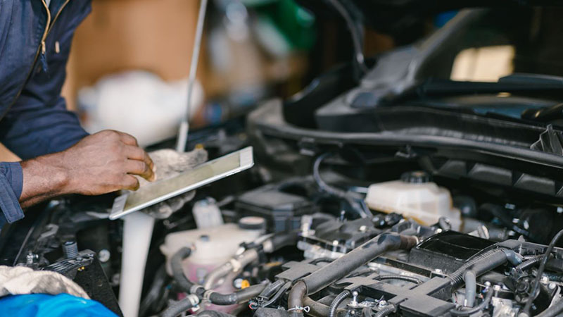 Mechanic using a tablet to diagnose and check car engine ECU in a workshop.