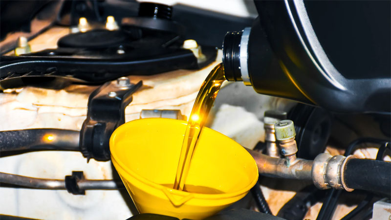 Aceite de motor nuevo vertido en un embudo amarillo durante el cambio de aceite: mantenimiento del automóvil y protección de la bomba de aceite.