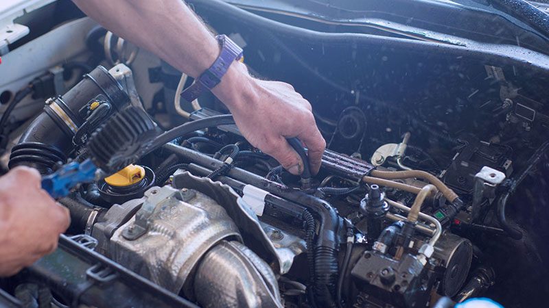 Auto mechanic working under the hood, repairing a car engine. Selective focus on hands and tools.