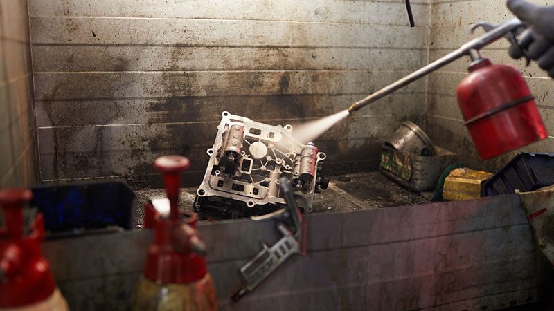Repairman sandblasting a car engine part to remove debris and clean the surface during engine restoration.