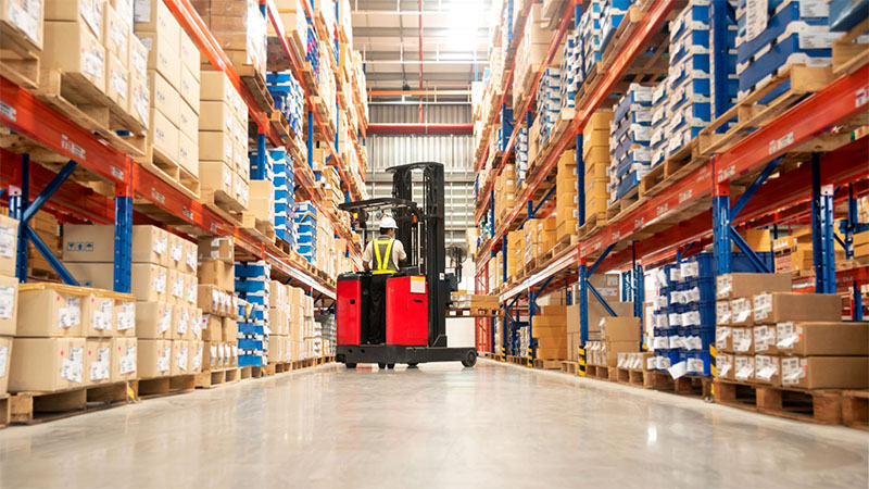 Forklift worker loading packed goods in a large distribution warehouse with high storage shelves.