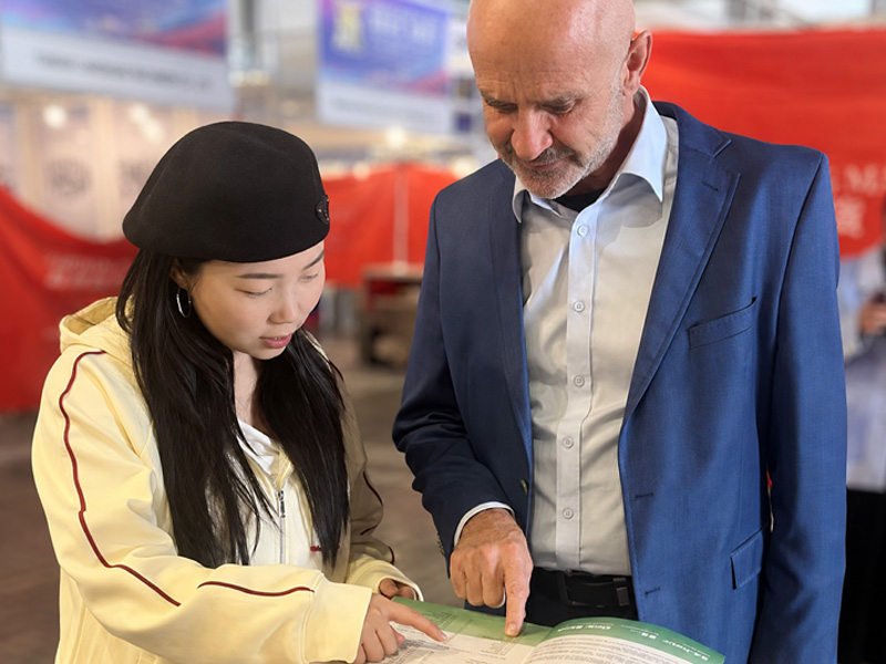 Woda Auto staff reviewing engine product catalog with customers at an auto parts trade show.