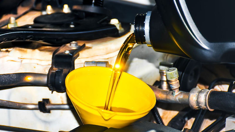 Engine oil being poured into engine through funnel during oil change.