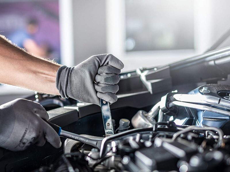 Auto mechanic working on and repairing a car engine in a professional workshop.