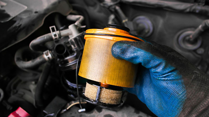 Gloved hand holding a diesel engine fuel filter during replacement.