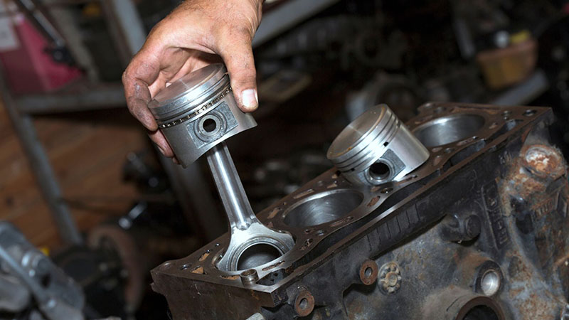 Mechanic holding pistons with connecting rods removed from a diesel engine.