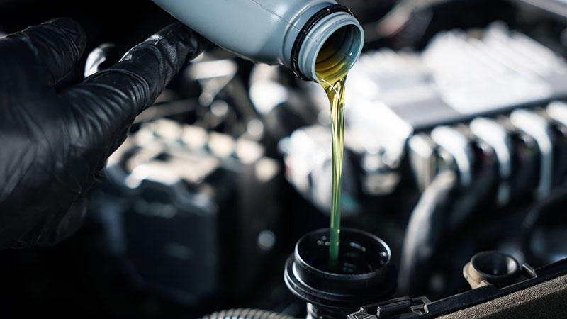Close-up of a mechanic pouring fresh motor oil into a vehicle engine.