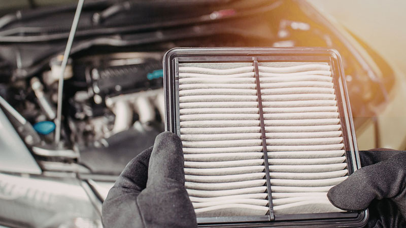 Mechanic holding a car air filter during vehicle engine maintenance and replacement service.
