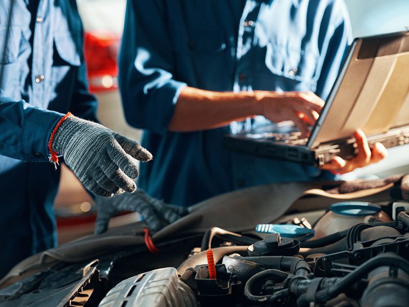 Hands of auto mechanics repairing a car engine during maintenance at a professional service workshop.