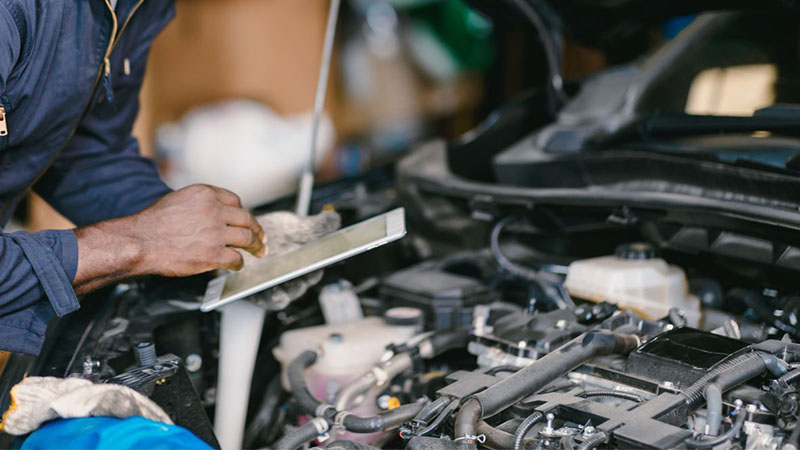 Garage mechanic using a tablet computer to check and tune a car engine ECU during professional auto service.