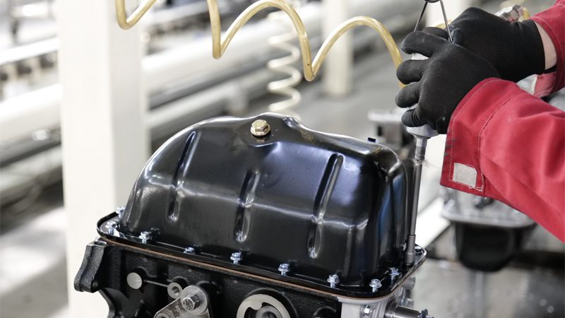 Mechanic installing an engine oil pan on an internal combustion engine at the production line of Nanjing Woda Auto Technology Co., Ltd.