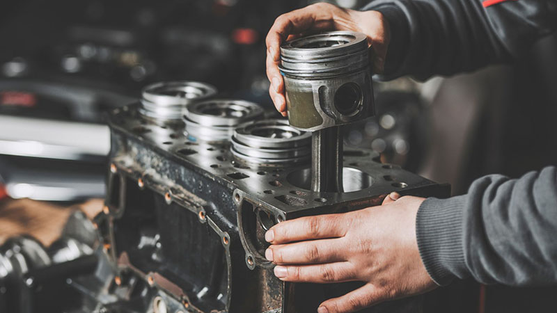 Mechanic performing engine piston repair on a car engine.