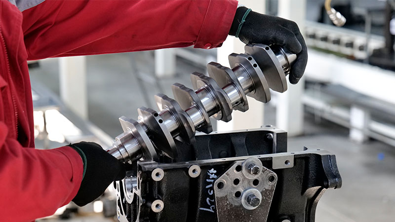 Mechanic installing a crankshaft into an engine block on the engine assembly line at Woda Auto factory.