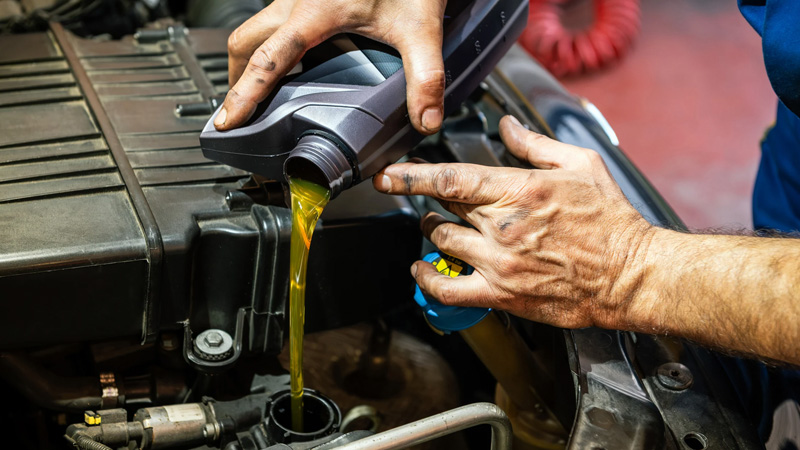 Mechanic pouring engine oil into a Nissan diesel engine during routine maintenance.