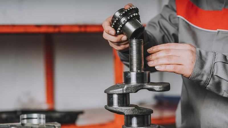 Mechanic working on a crankshaft, performing inspection or maintenance on engine components.